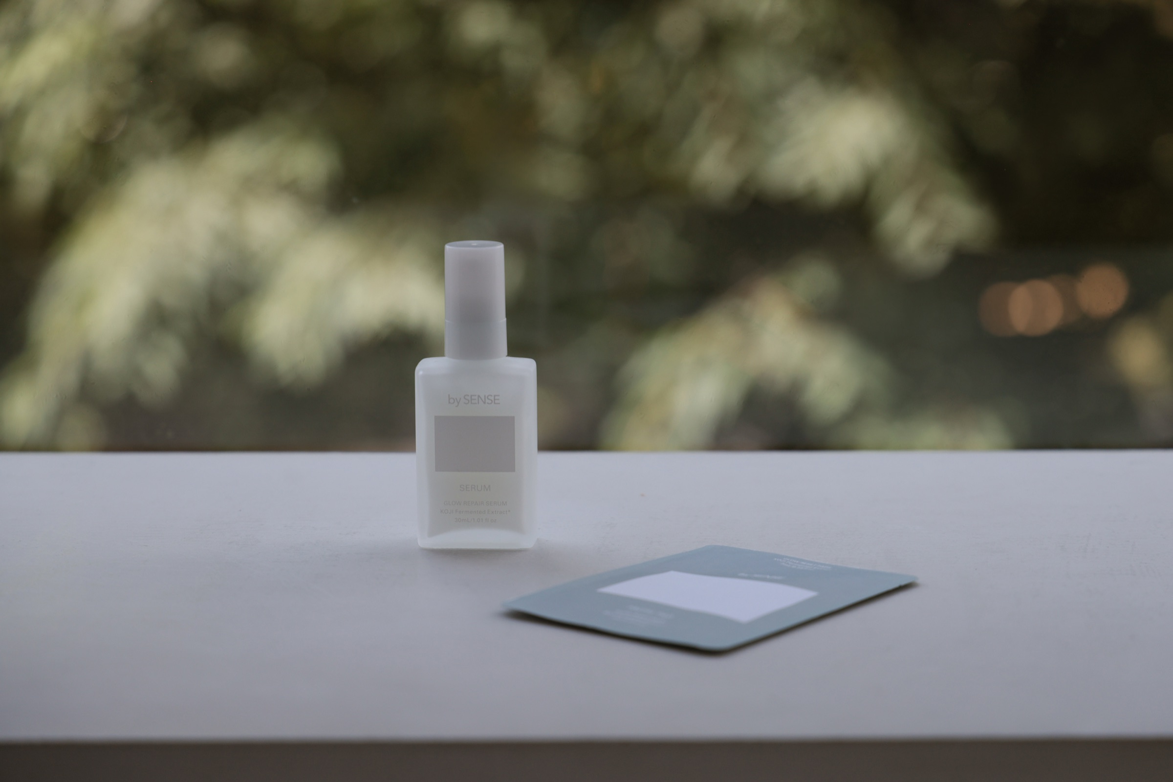 白いテーブルに置かれた bySENSE の美容液と、緑のボケが広がる明るい空間