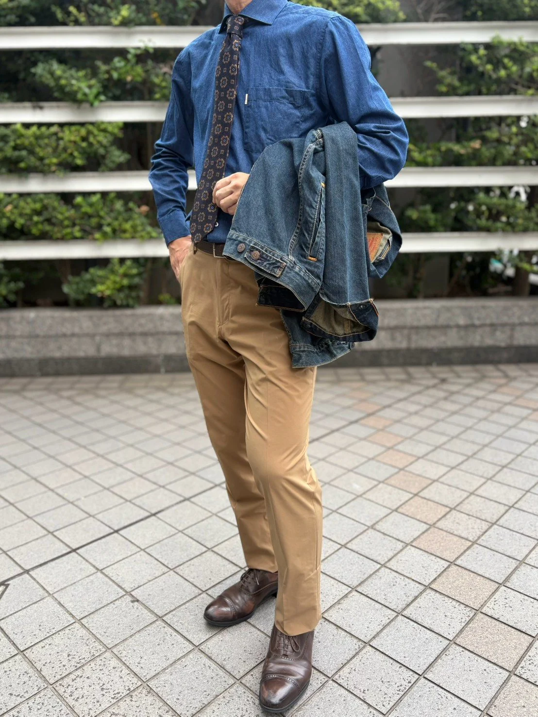 ブルーのデニムシャツにネクタイを結びジャケットを手に持つ着こなし
