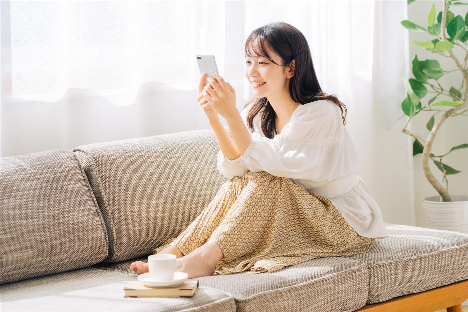 ソファでスマートフォンを操作する女性