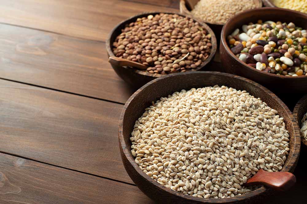 木製のボウルに盛られた大麦やレンズ豆などの様々な雑穀と豆類の画像