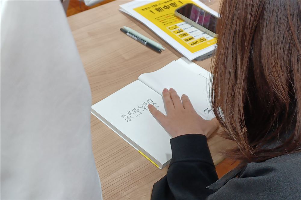 たまさんの書籍にサインをしてもらう参加者の手元