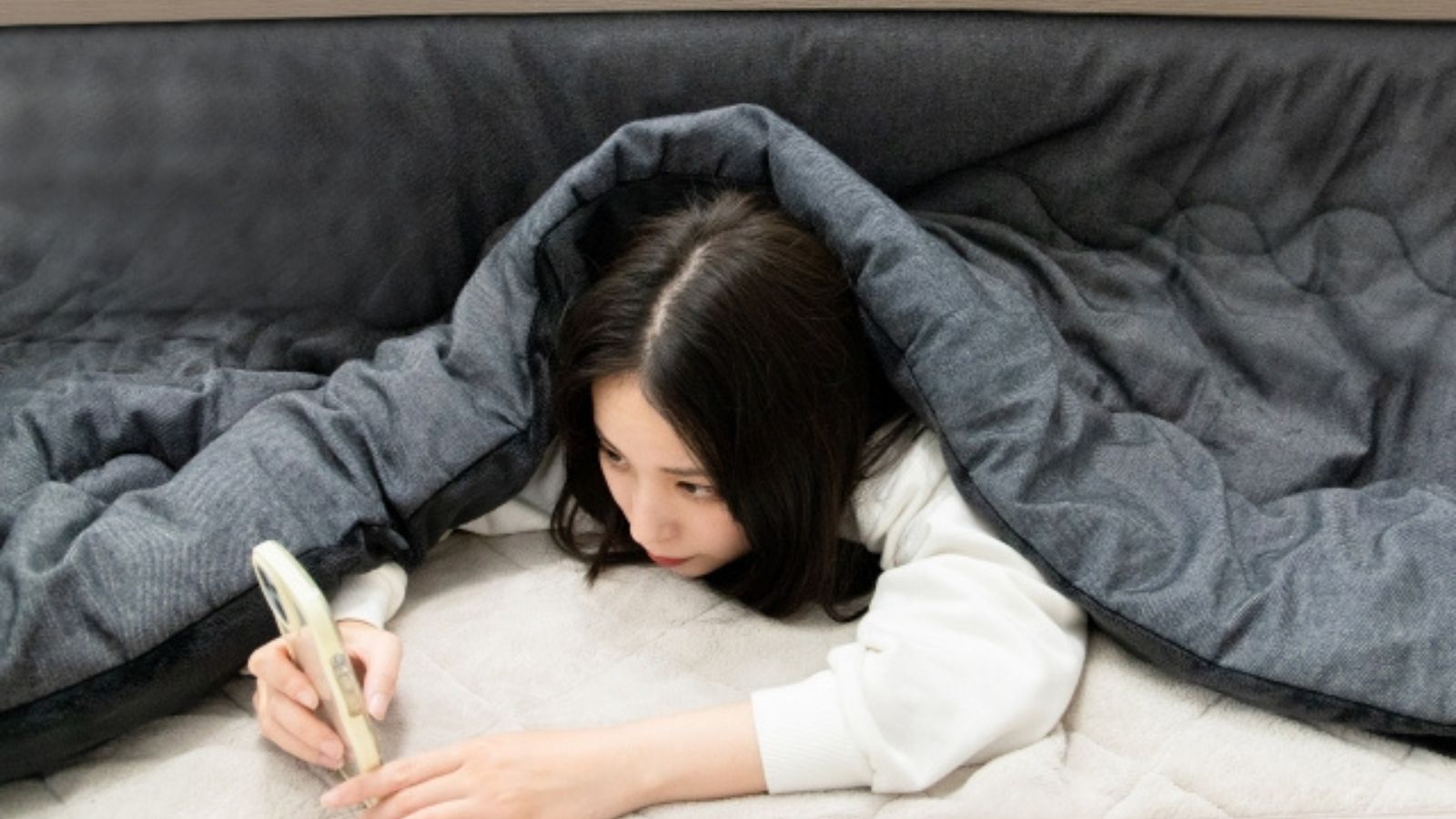 こたつでスマホを見ている女性