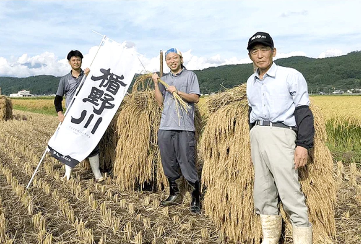 稲刈りを終えた田んぼで、楯野川ののぼりを手にする蔵人と農家さん
