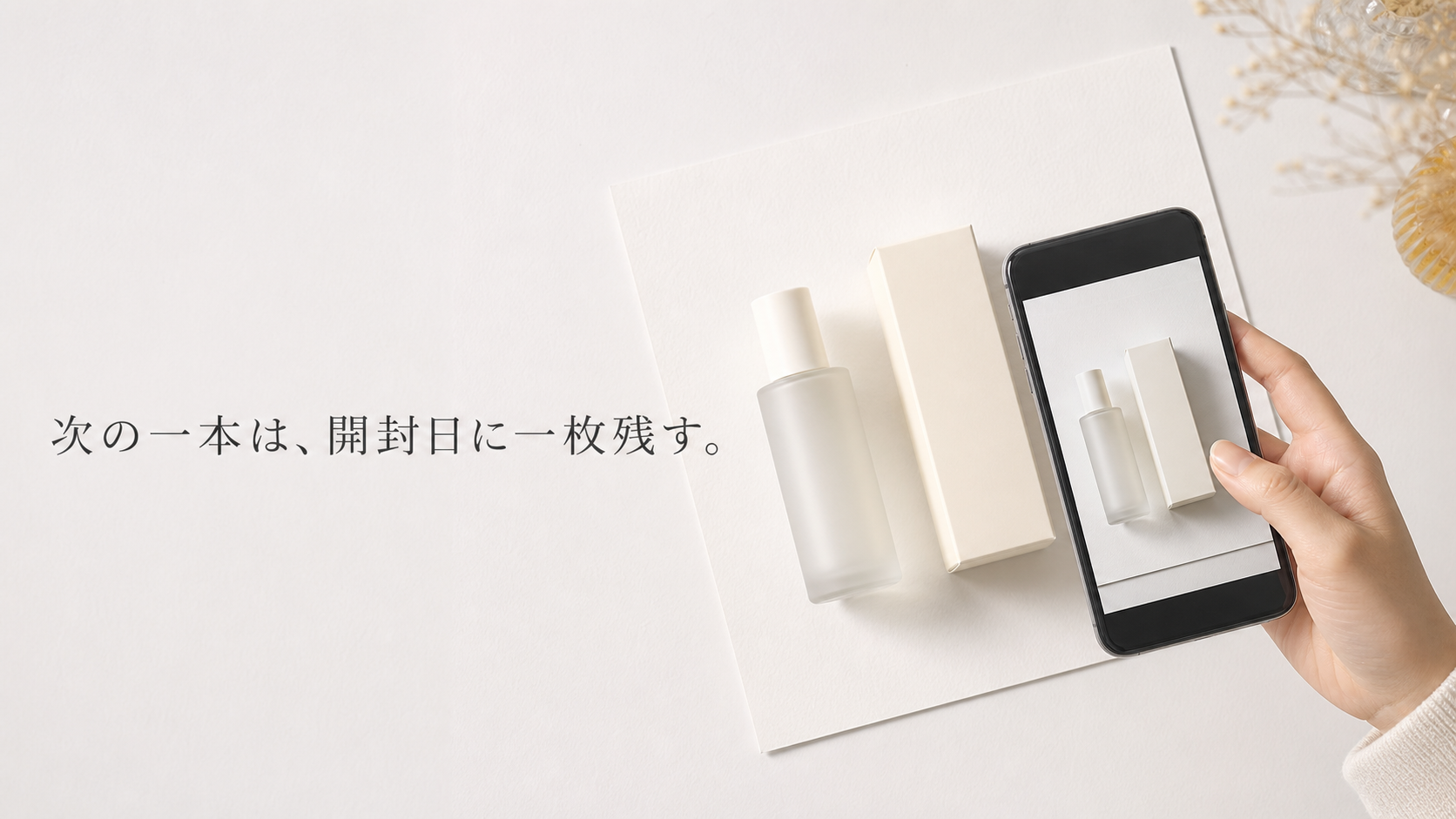 白い背景に新しい無地ボトルと外箱を置き、自然な手がスマートフォンで開封日の一枚を撮る真上写真