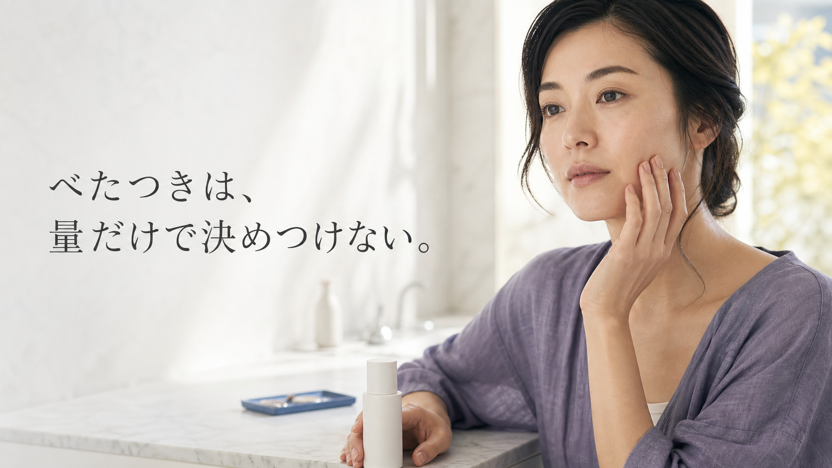 洗面スペースで頬へ軽く手を添え、美容液を塗った後の感触を静かに確かめる女性の写真