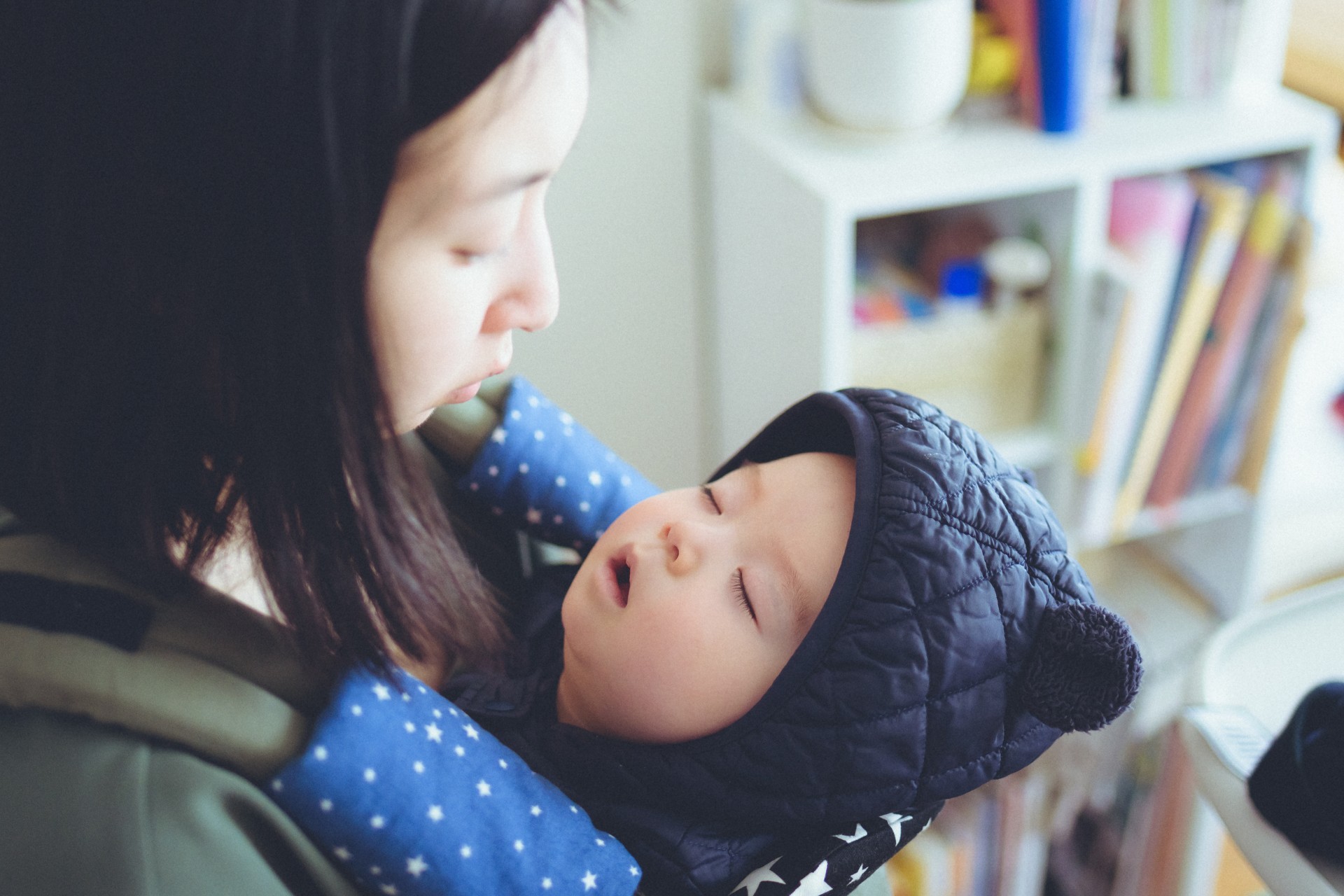 子育て中のママが、抱っこ紐で眠る子供を優しく抱いている様子